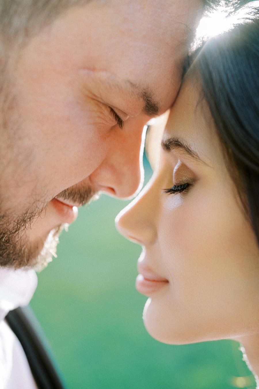 Close-up of a loving couple with foreheads touching, eyes closed, surrounded by soft natural light, conveying romance and intimacy.
