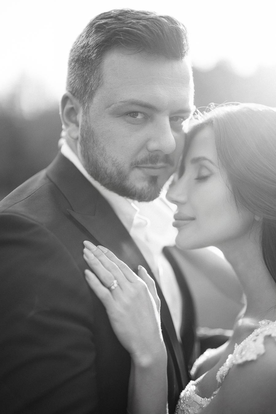 Black and white close-up portrait of a couple embracing, showcasing an engagement ring on the woman's hand against a soft, blurred background.