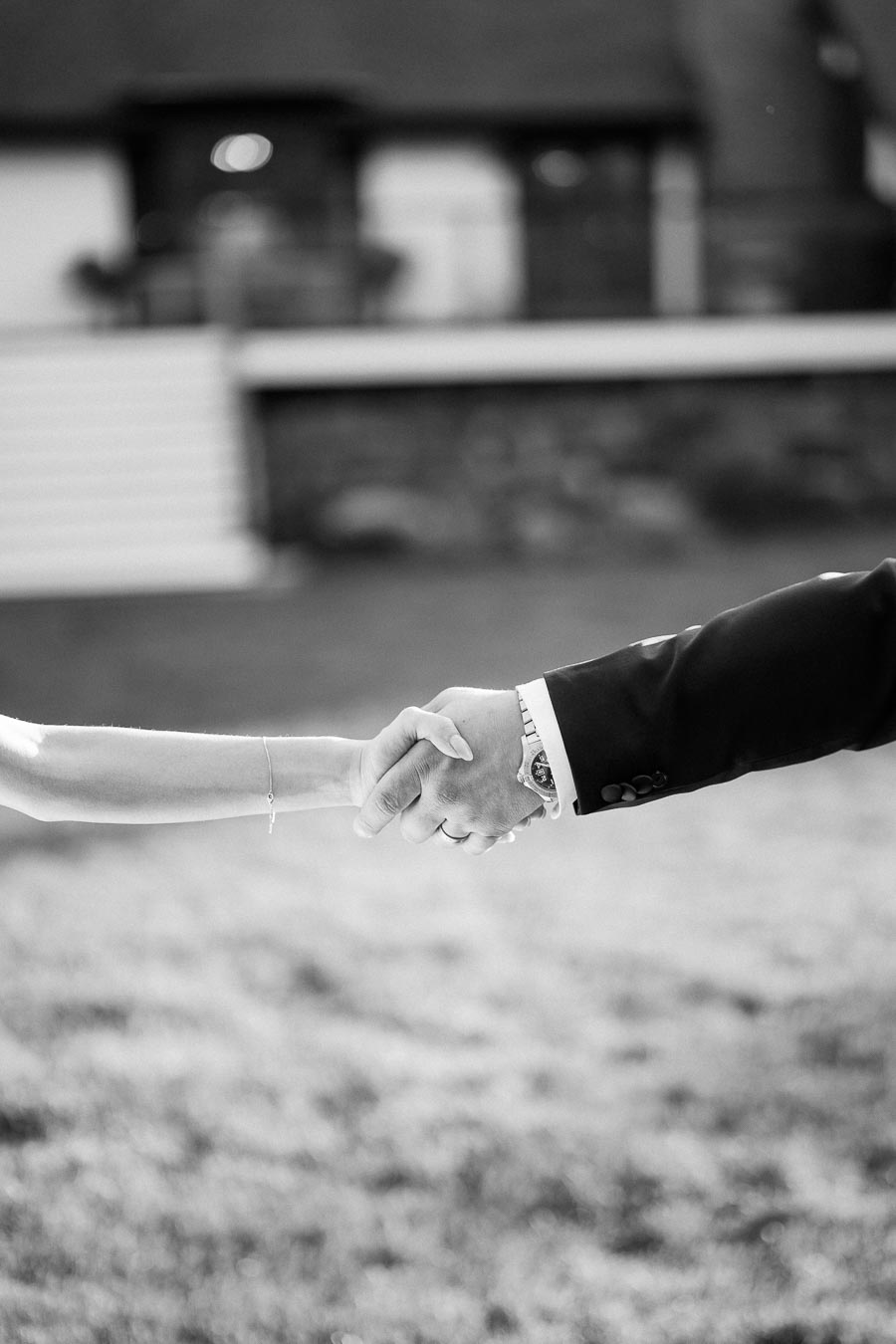 Black and white photo of a couple holding hands outdoors, symbolizing love and connection, with a blurred background of a building and grass.