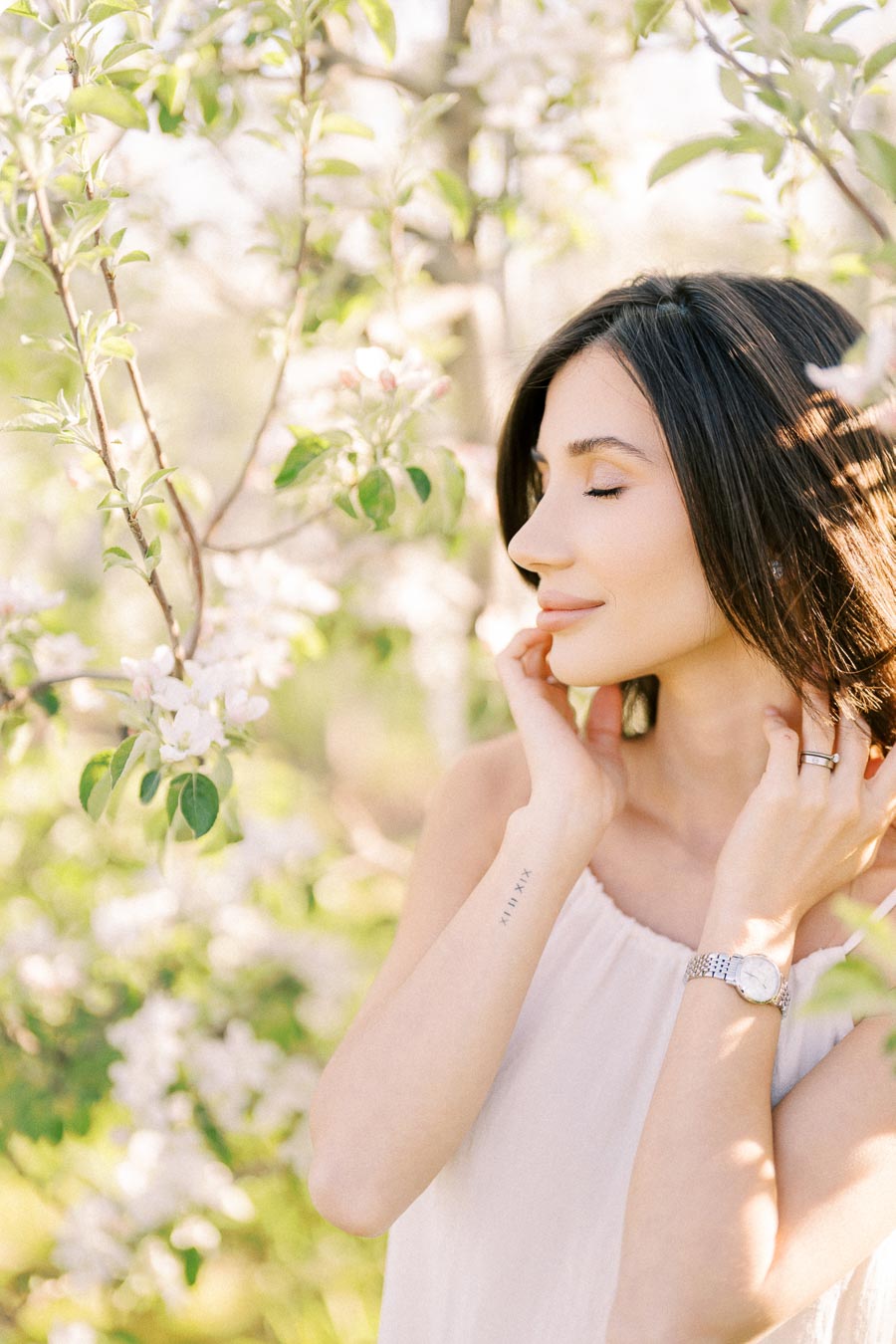 Woman enjoying nature in a blooming garden, surrounded by white flowers and lush green leaves, with sunlight glowing through the trees.