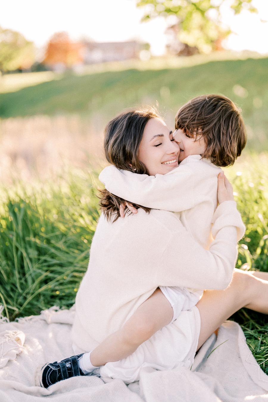 A mother and child share a warm embrace while sitting on a blanket in a sunlit meadow, capturing a moment of pure joy and love in nature.