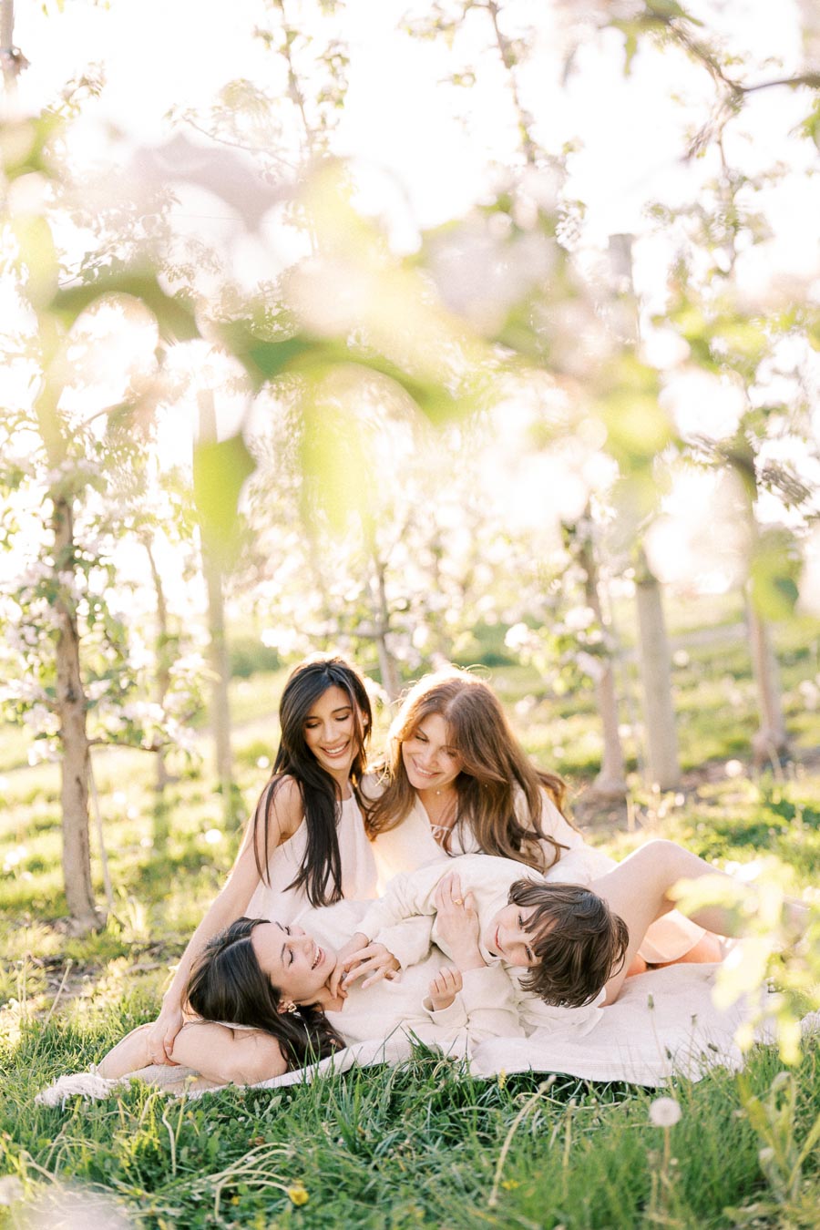 A group of women and a child enjoying a sunny day in an orchard, surrounded by blossoming trees and lush green grass, creating a warm and joyful atmosphere.