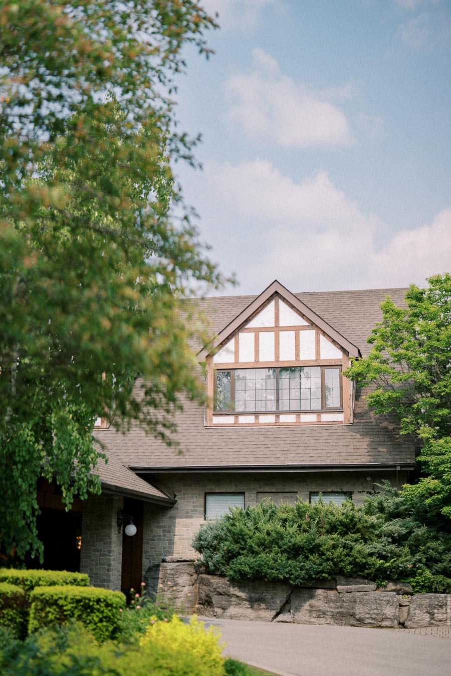 Charming Tudor-style house with wooden beams and stone exterior surrounded by lush greenery and a clear blue sky in the background.