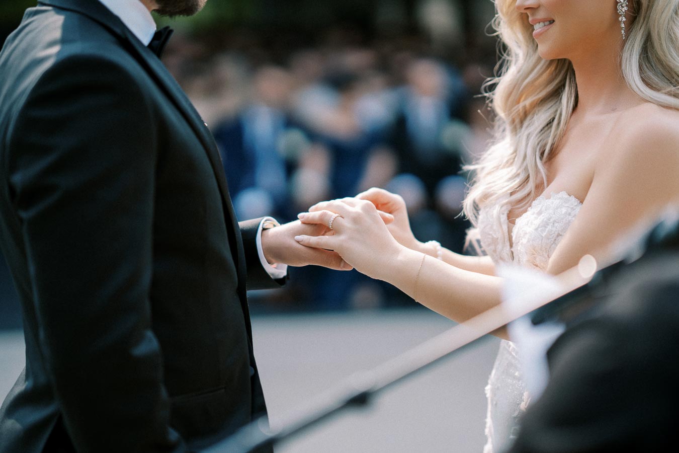 Wedding ceremony close-up of bride placing ring on groom's finger, both in elegant attire, symbolizing love and commitment.
