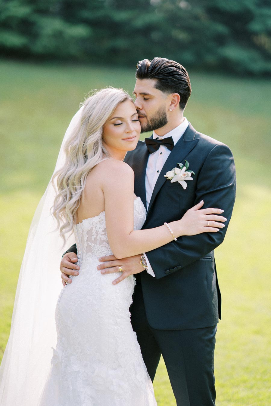 Elegant bride and groom embracing in a sunlit garden setting, showcasing a lace wedding dress and classic tuxedo.
