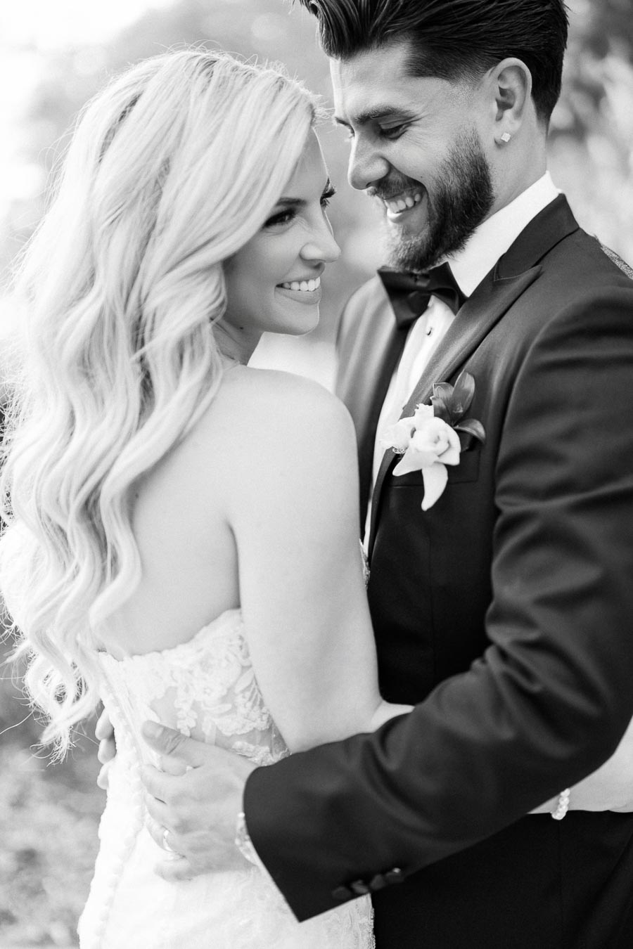 A black and white photo of a smiling bride and groom embracing outdoors, capturing a joyful moment on their wedding day.