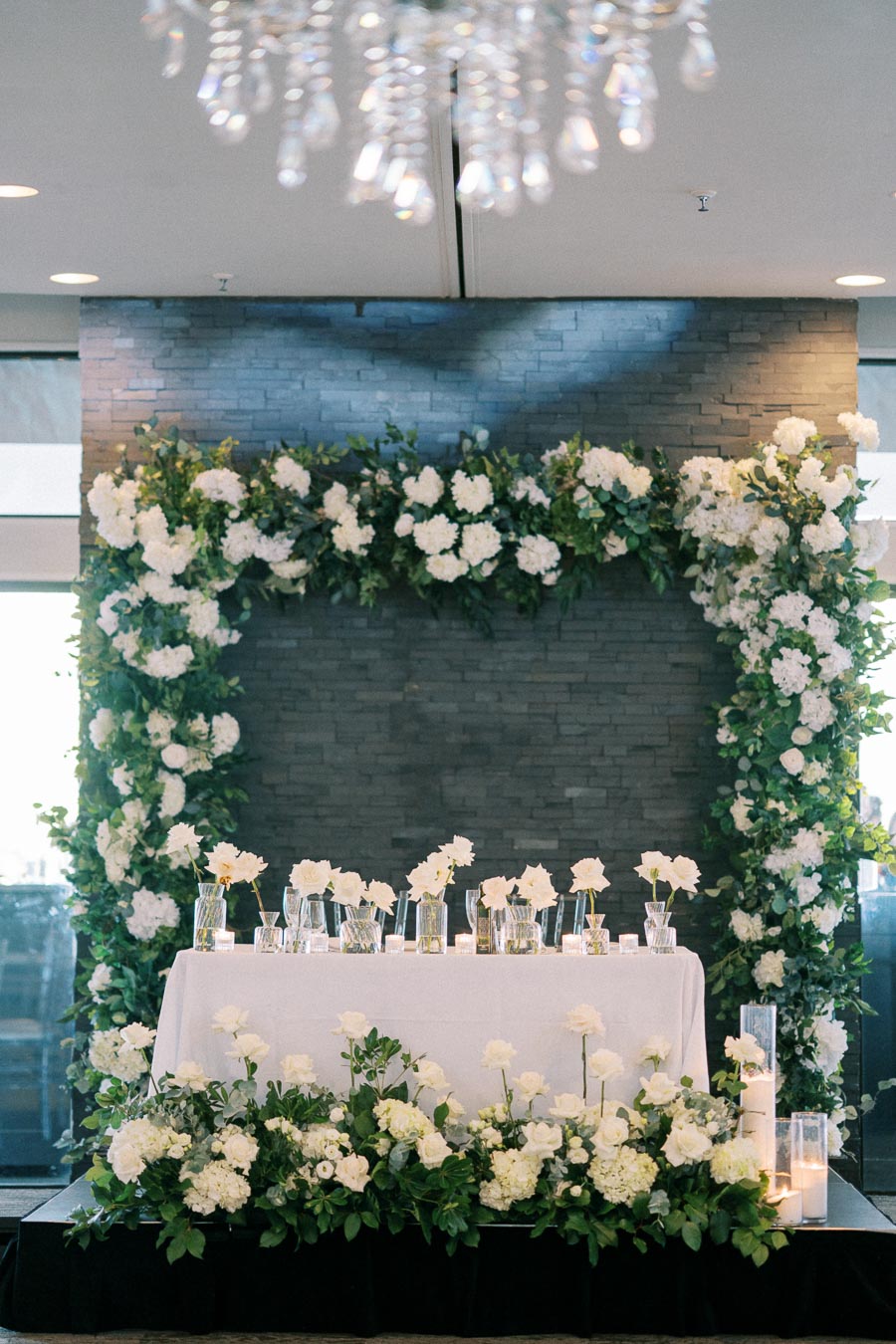 Elegant wedding reception with a floral arch and candlelit table adorned with white roses and hydrangeas, creating a romantic atmosphere.