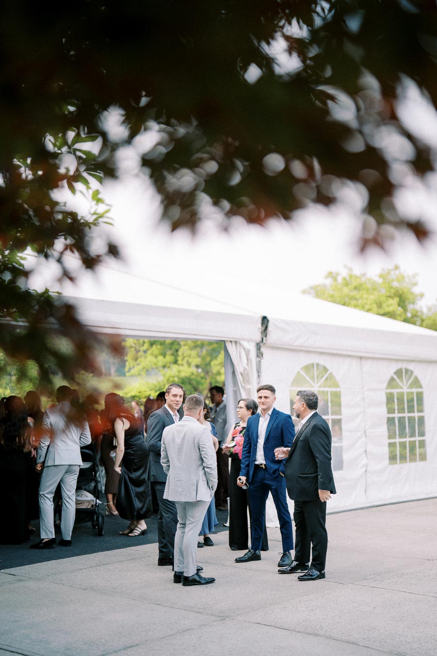 Outdoor formal event with people socializing near a white tent.