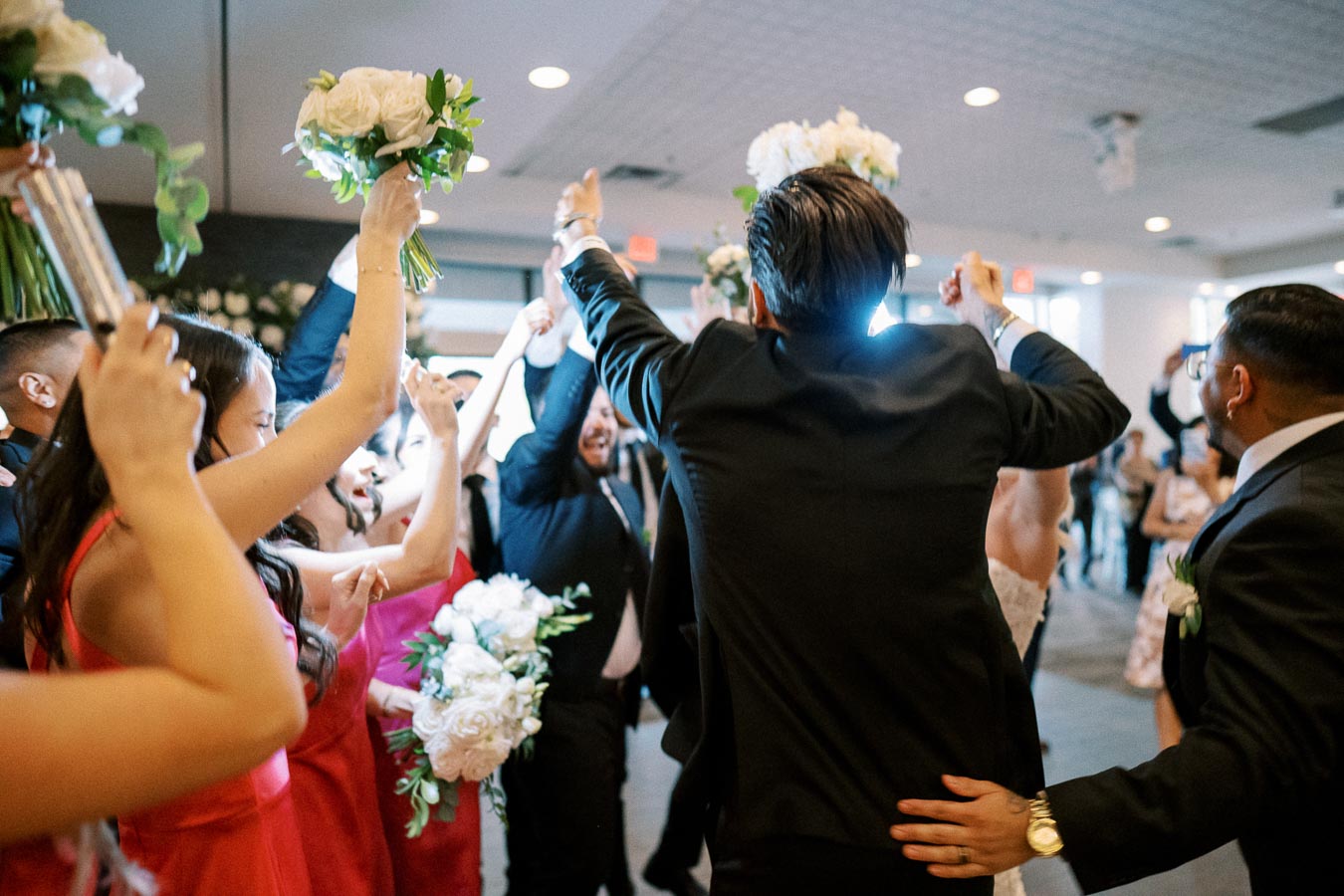 Group of people celebrating at a wedding reception, wearing formal attire and holding floral bouquets, with a joyful atmosphere.
