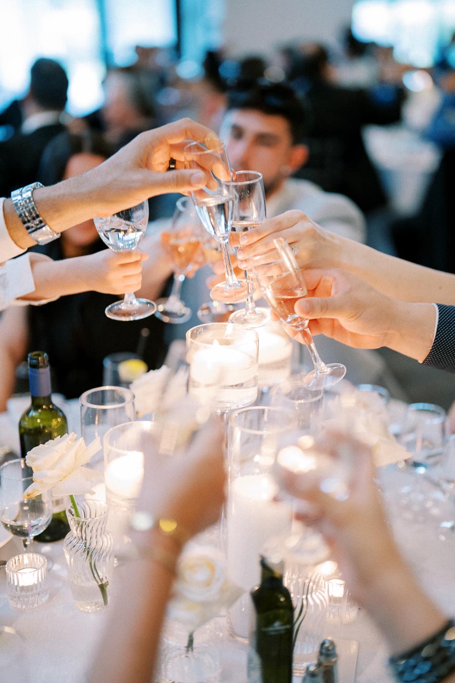 Group of people raising champagne glasses in a celebratory toast at an elegant event with a candlelit table setting.