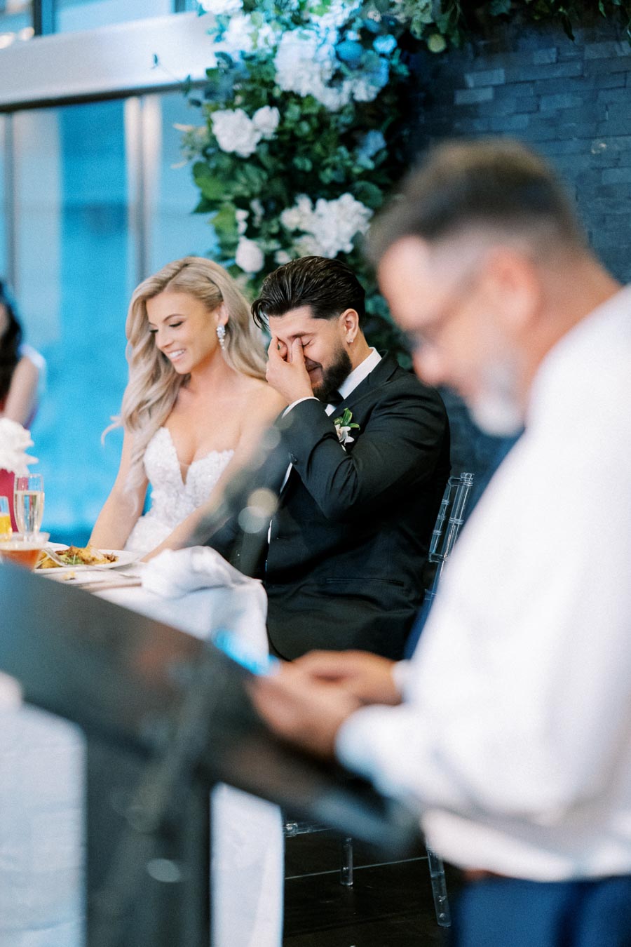 Emotional wedding moment with bride and groom reacting to heartfelt speech, surrounded by elegant floral decorations.