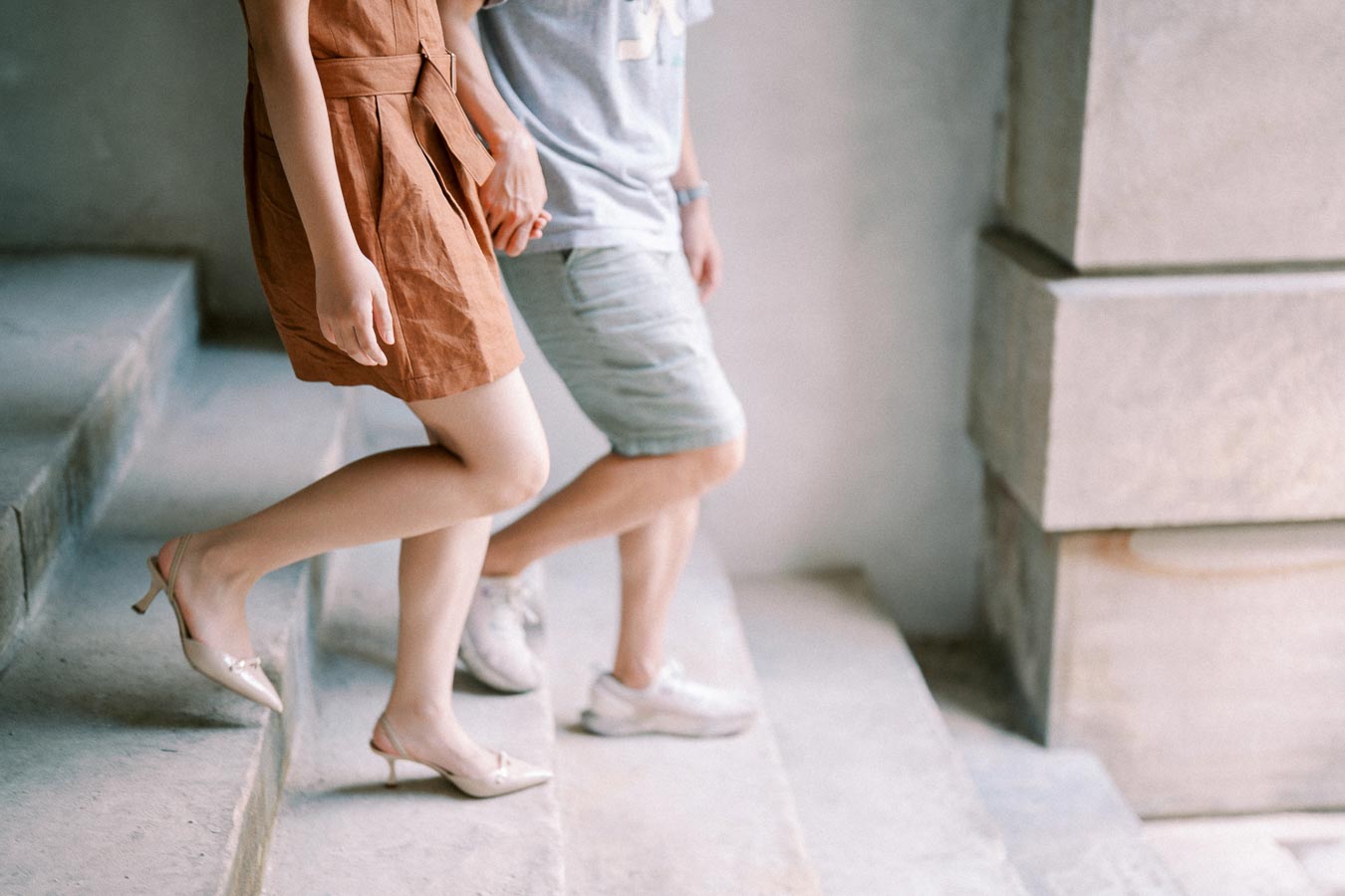 A couple descends a set of concrete stairs, with the woman in a brown dress and heels, and the man in casual attire.
