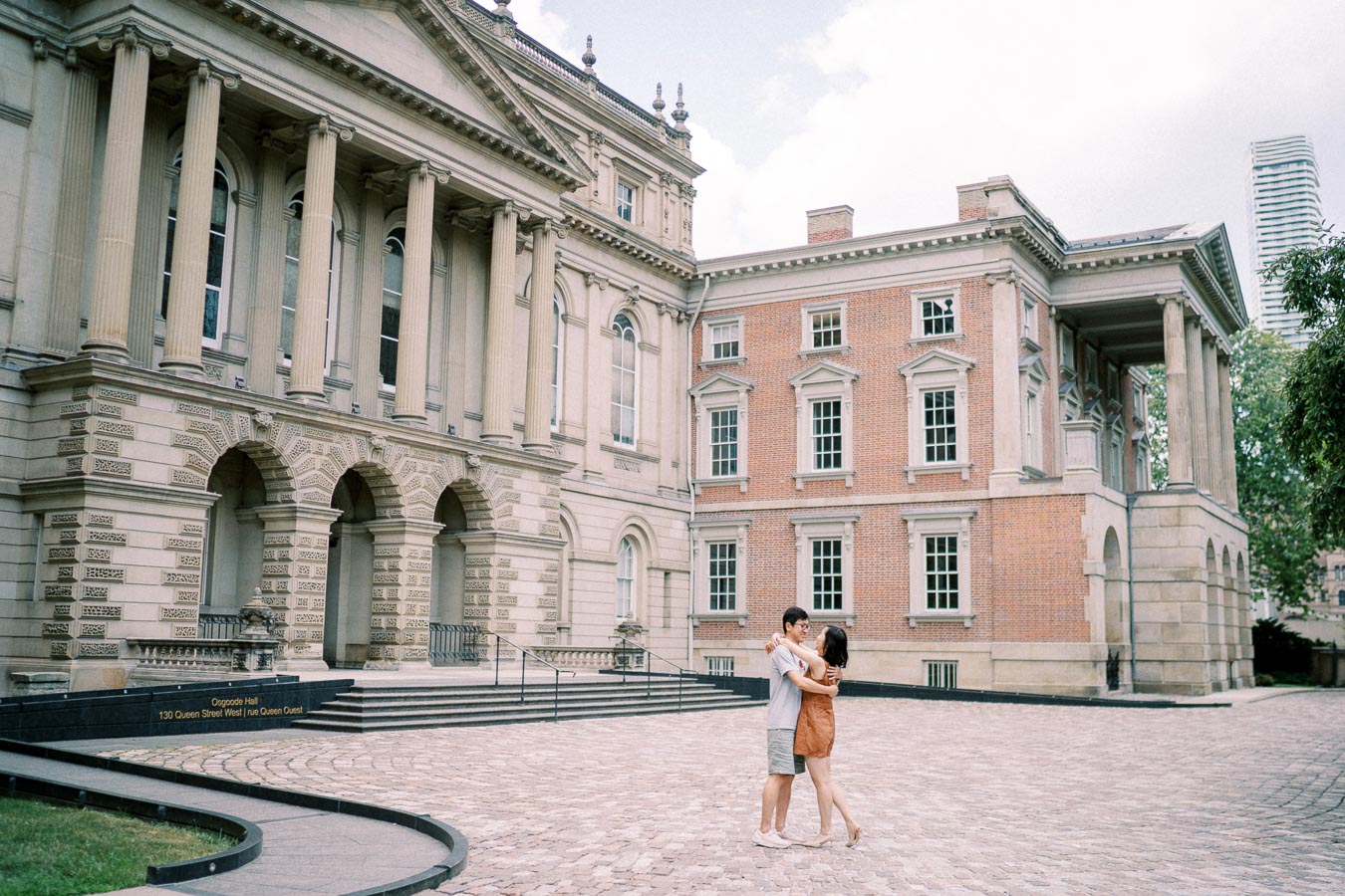 Couple embracing in front of the historic Osgoode Hall building in Toronto, with full architecture view