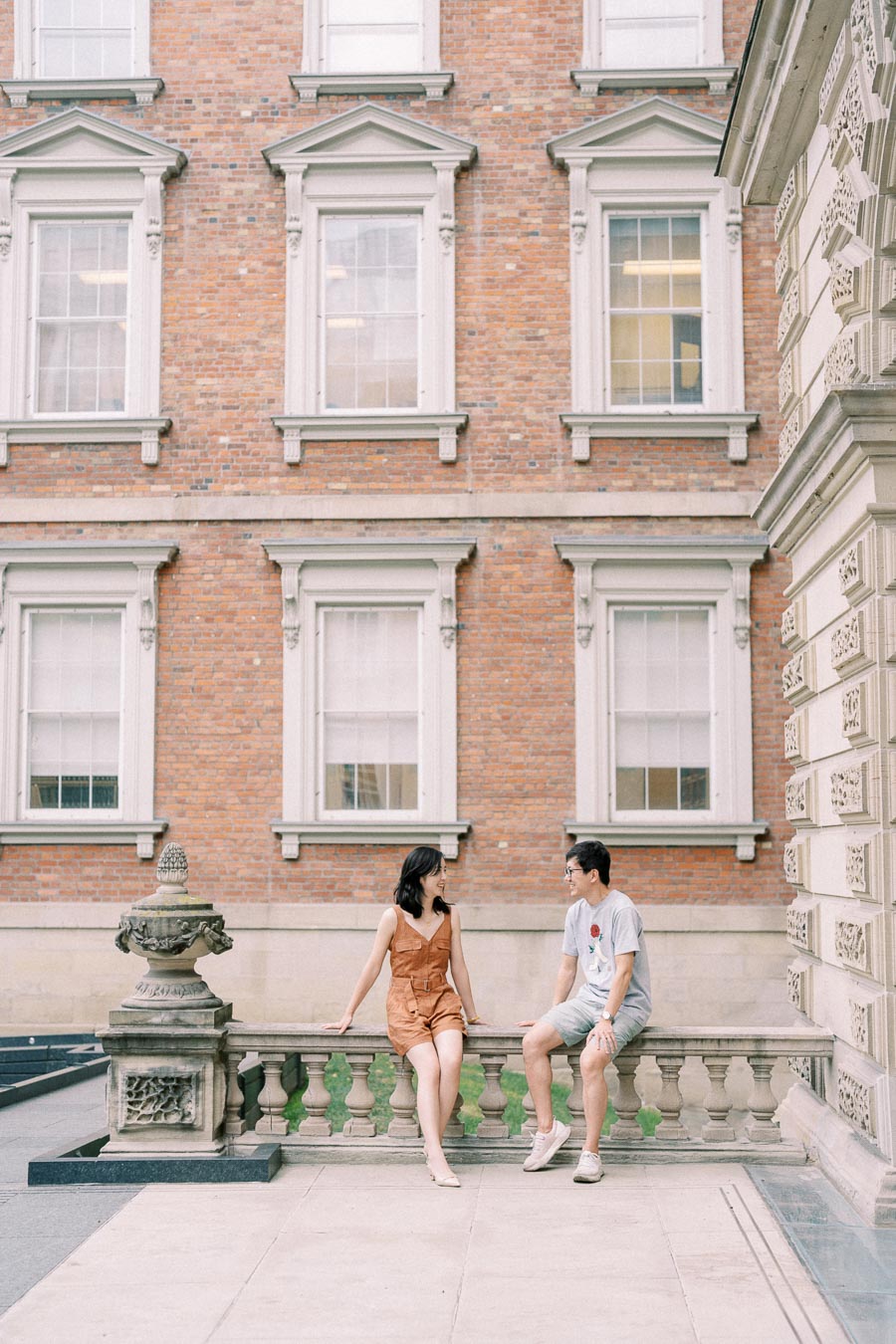 A couple enjoys a moment together in front of a historic brick building with ornate white-framed windows.