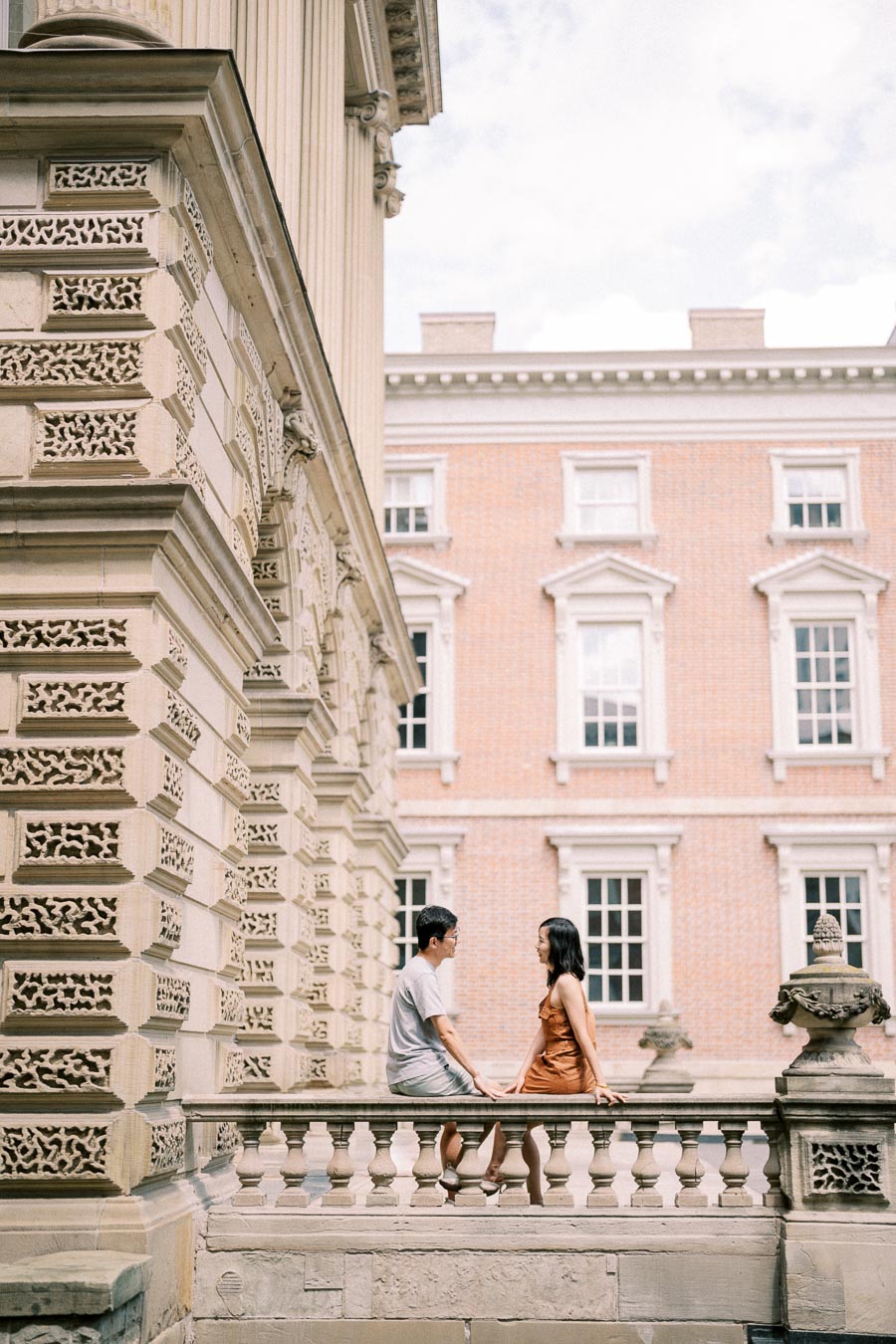 A couple enjoys a moment together on a stone balustrade, surrounded by the ornate architecture of a historic building.