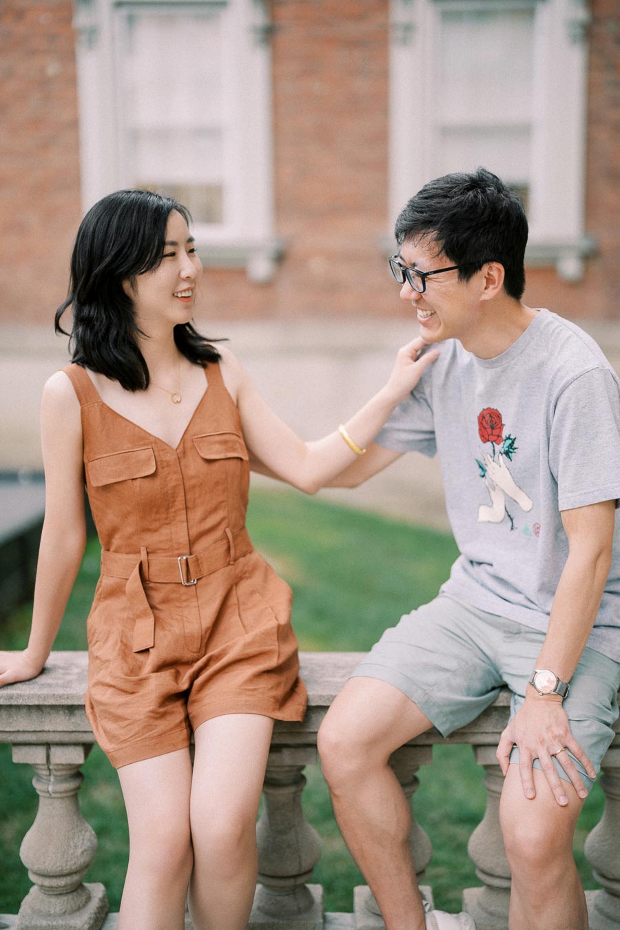 A cheerful moment between two friends sitting on a stone railing, enjoying a conversation outdoors.