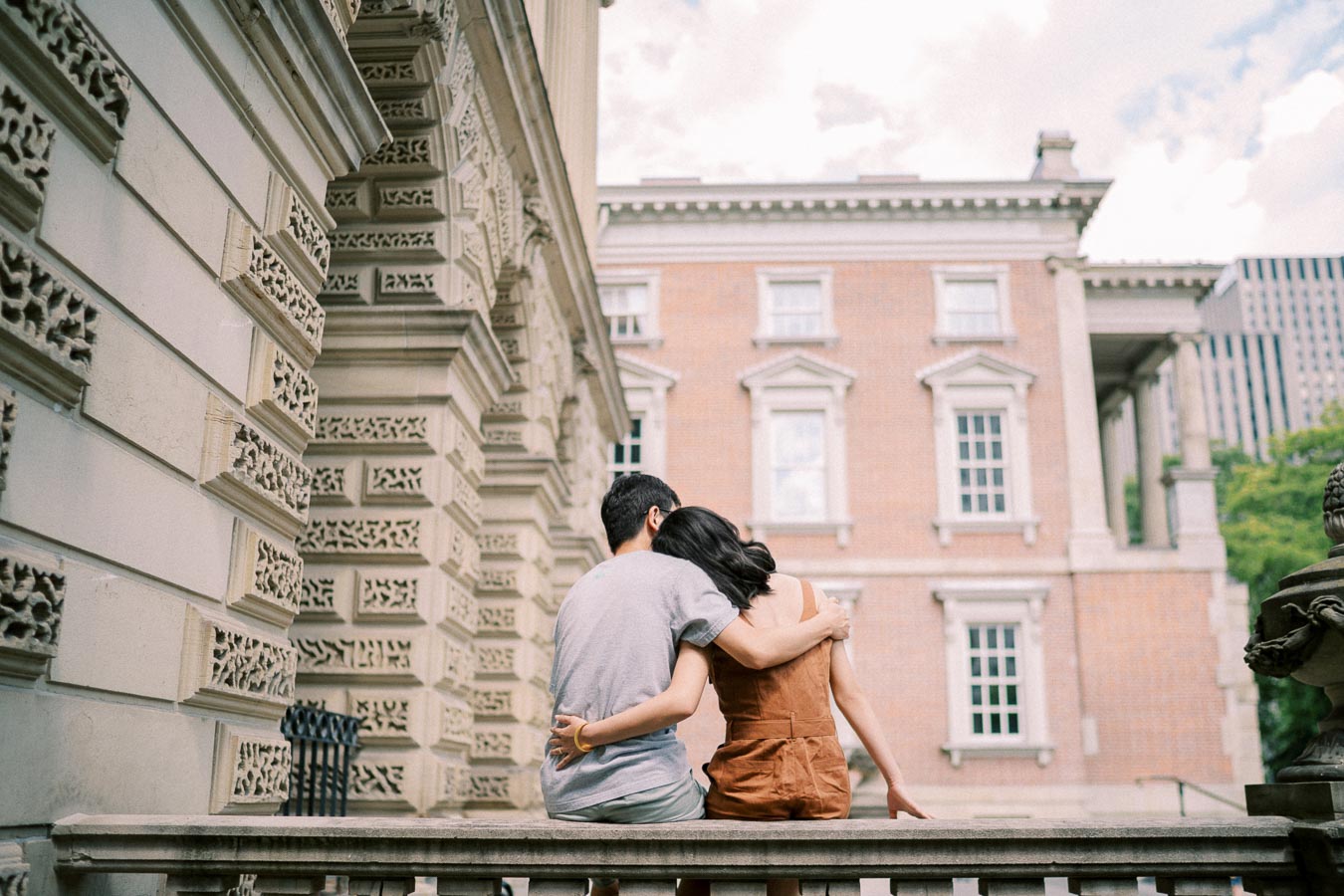 A couple embraces while sitting on a stone ledge in front of a historic building.