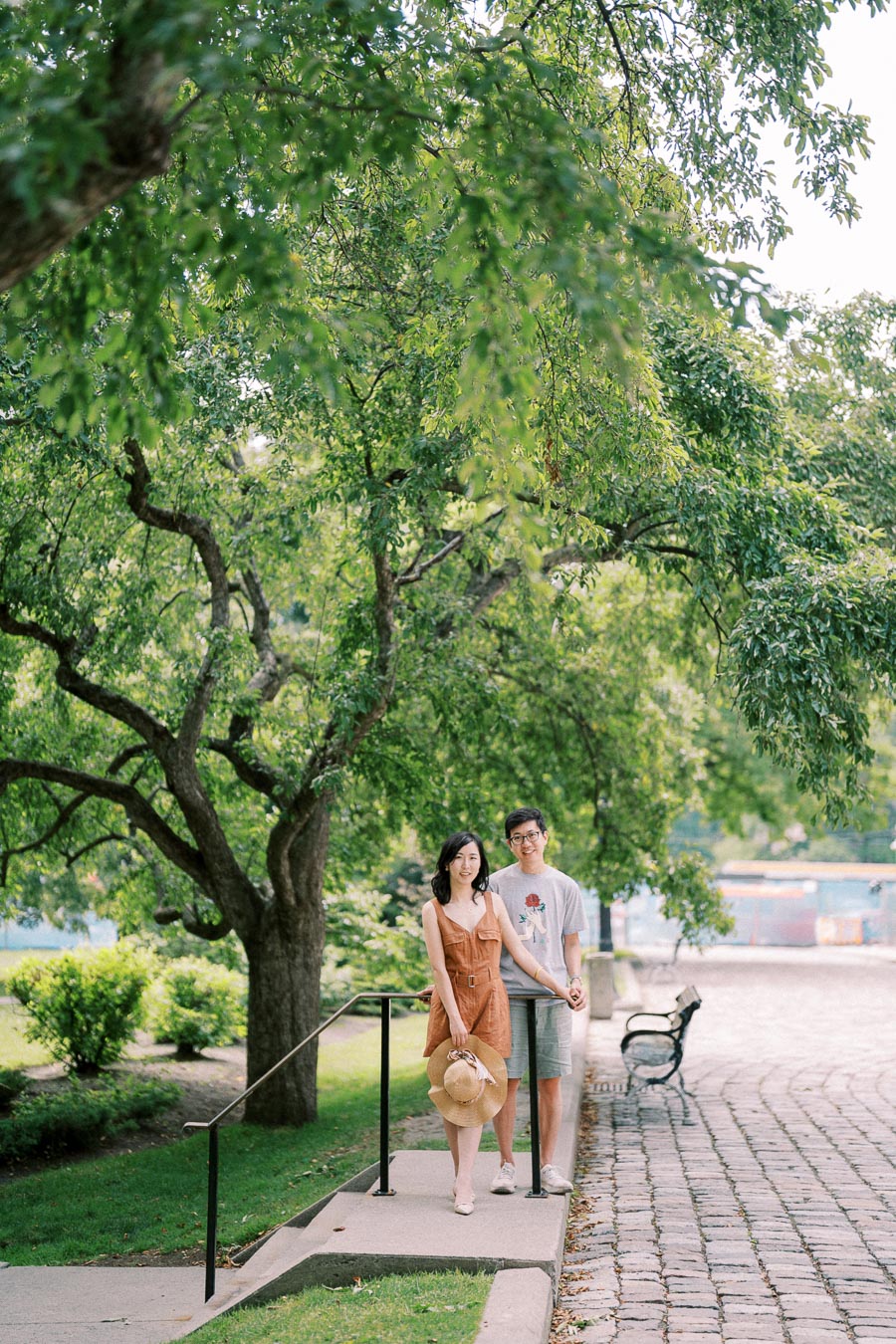 A couple enjoys a peaceful moment in a lush green park, standing on a cobblestone pathway.