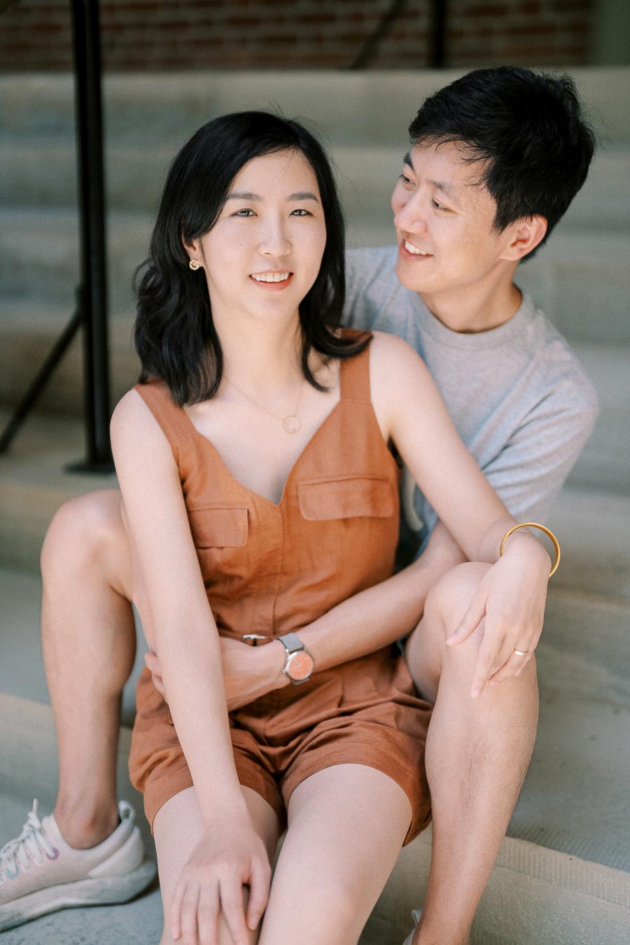 A couple enjoying a moment together on a staircase, with the woman wearing a brown dress and the man in a gray shirt.