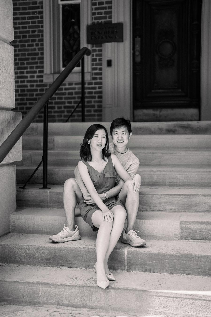 A couple poses on the steps of a brick building, enjoying a moment together.