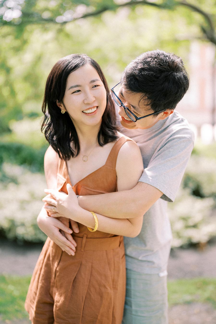 A couple shares a joyful moment in a sunny park, surrounded by greenery.