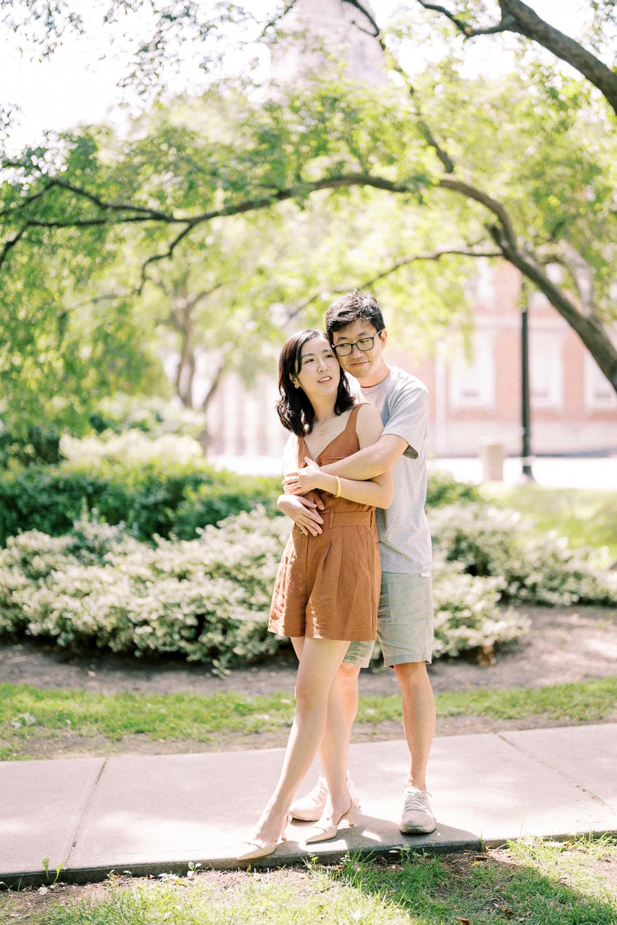 A couple enjoys a sunny day in the park, surrounded by lush greenery and a distant building.