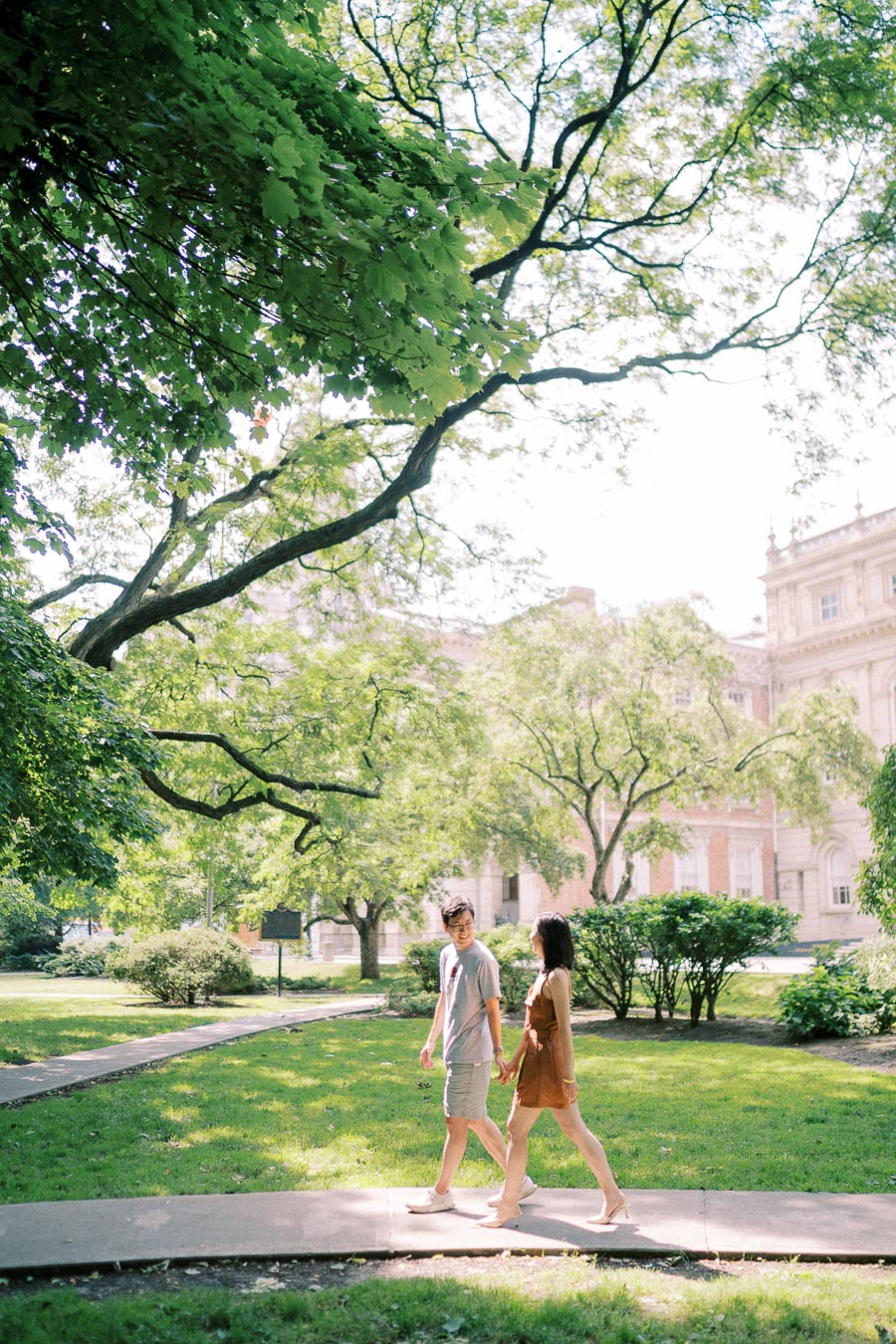 Couple walking hand in hand under trees at Osgoode Hall in Toronto