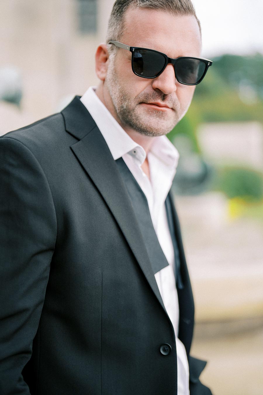 Confident man in a black suit and sunglasses outdoors, exuding style and sophistication.