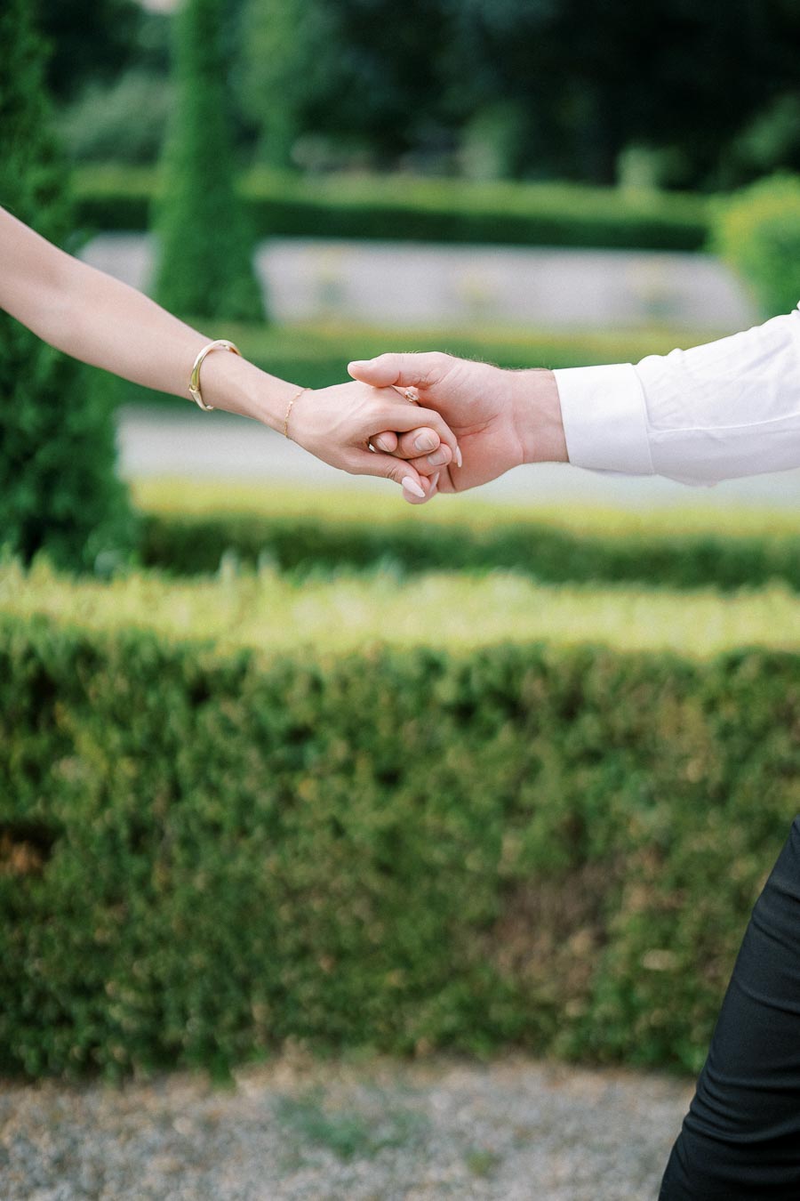 A couple holding hands outdoors in a lush green garden, symbolizing love and connection.