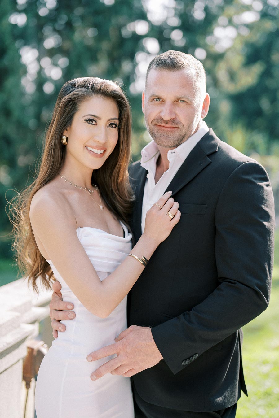 Couple posing affectionately in elegant formal attire with a lush green background