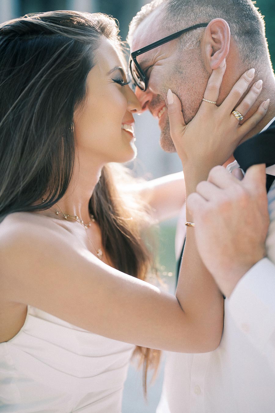 A couple smiling and embracing closely, showcasing a romantic and joyful moment in soft sunlight.