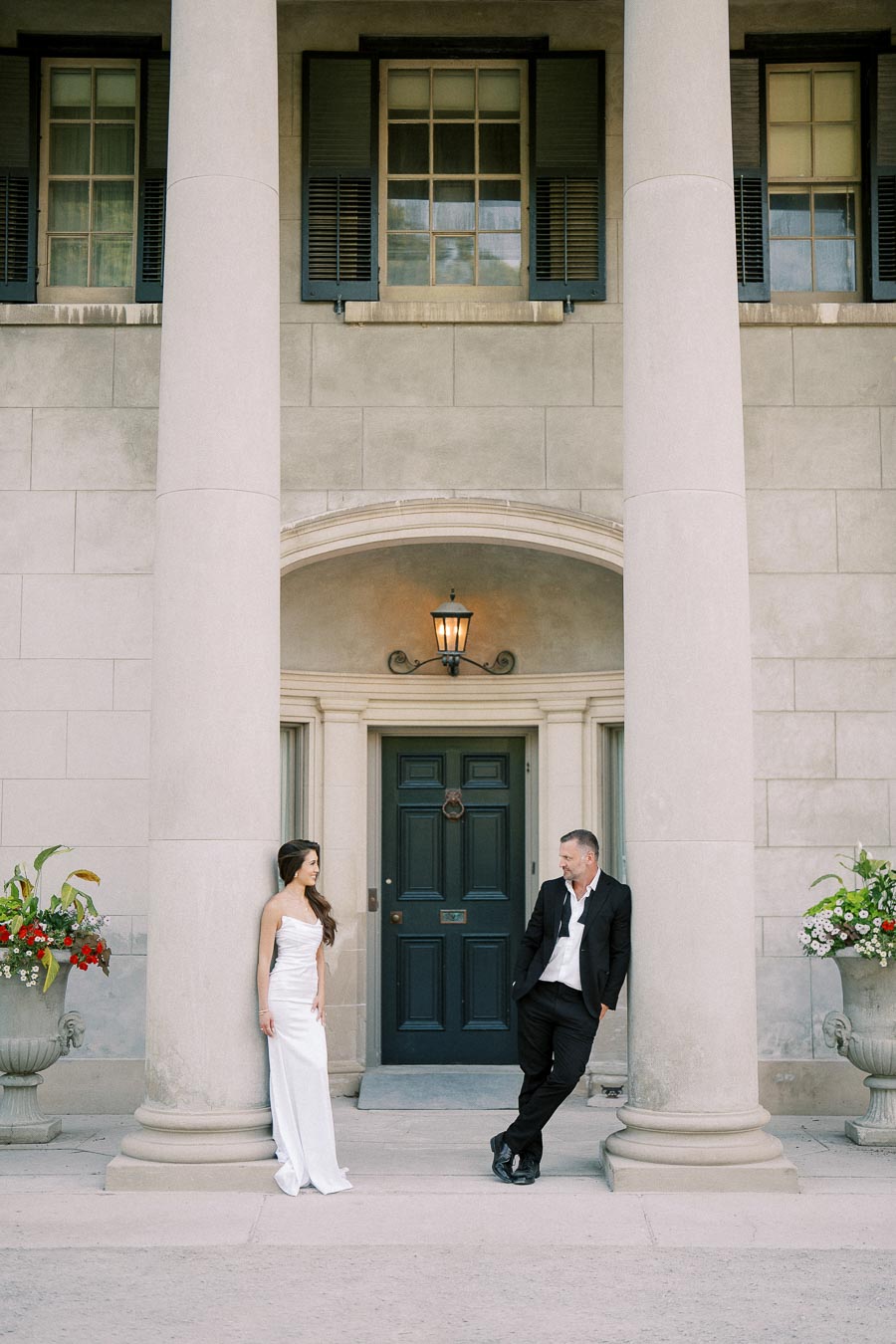 Elegant couple posing in front of a grand entrance with tall columns and floral arrangements, highlighting a classic architectural setting.
