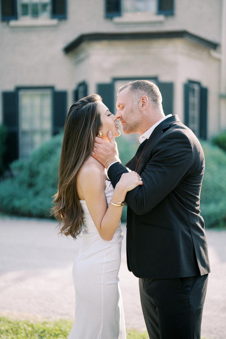 Engaged couple sharing a romantic moment outdoors in formal attire, with a historic building as the backdrop.