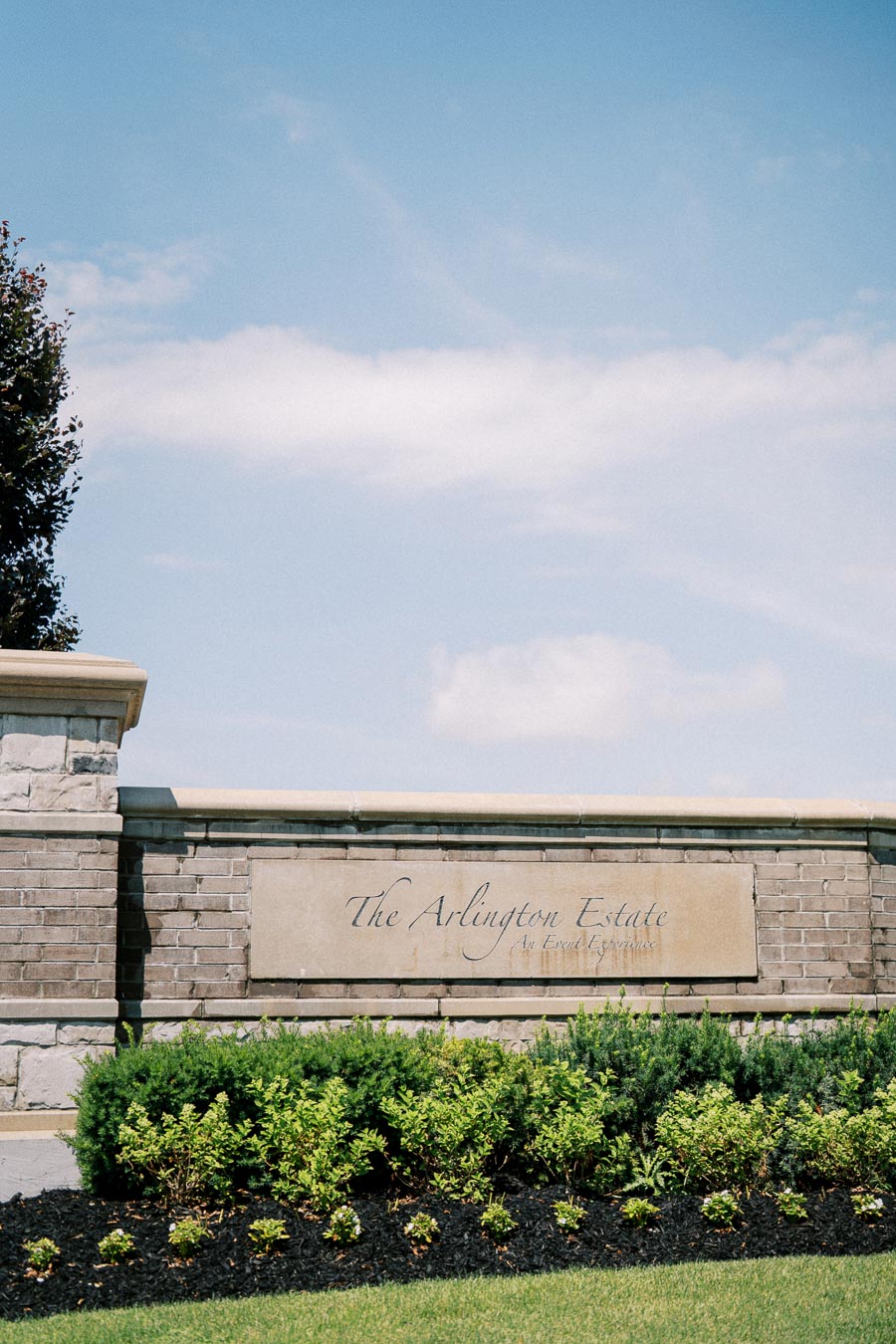 The Arlington Estate entrance sign surrounded by lush green landscaping and a clear blue sky.