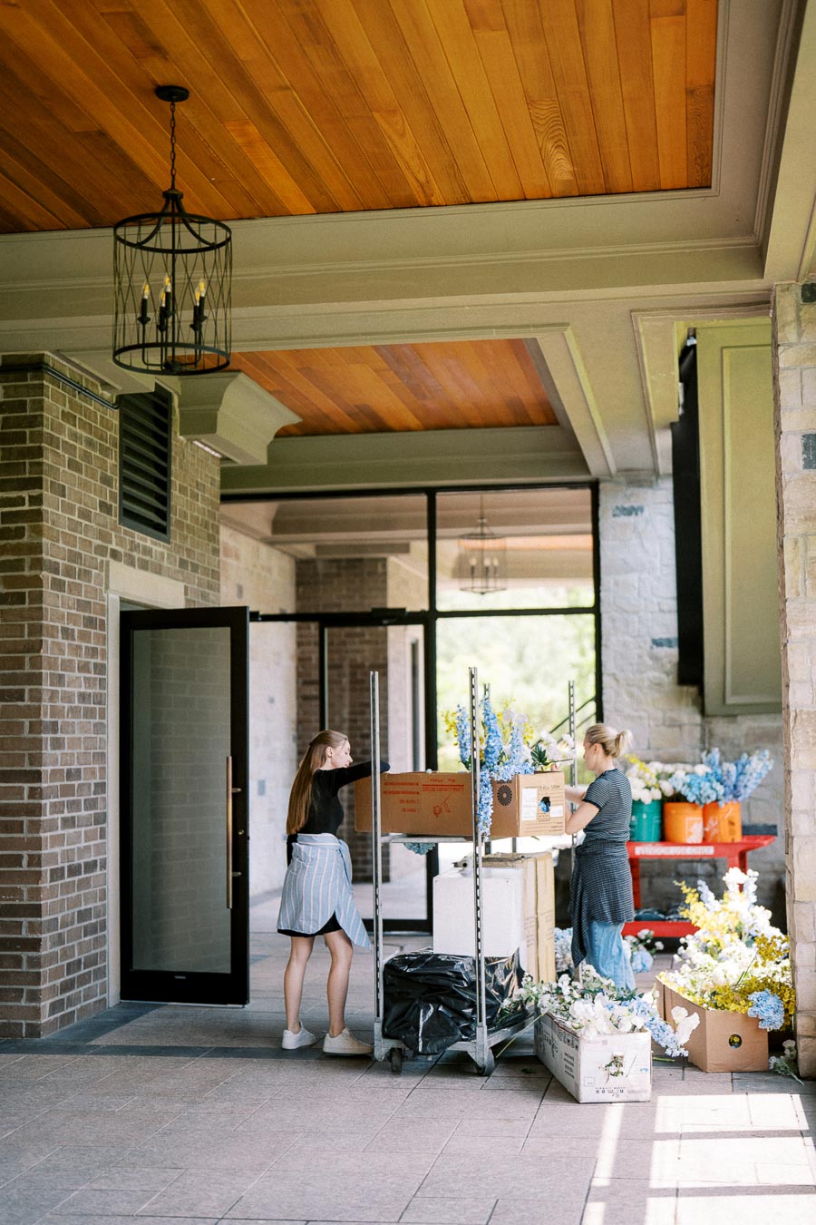 Florists arranging colorful bouquets in a covered outdoor space with a wooden ceiling and brick walls.