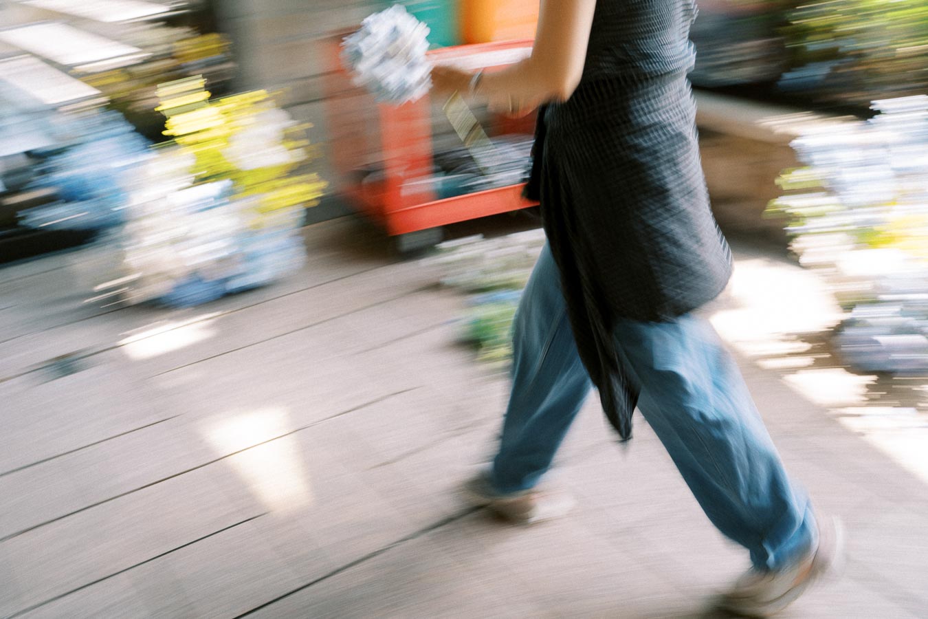 Blurry image of a person walking quickly while holding an item, with vibrant colors and motion effect in the background.