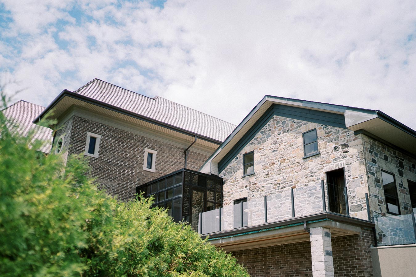 Historic stone and brick house with modern glass extension set against a partly cloudy sky.