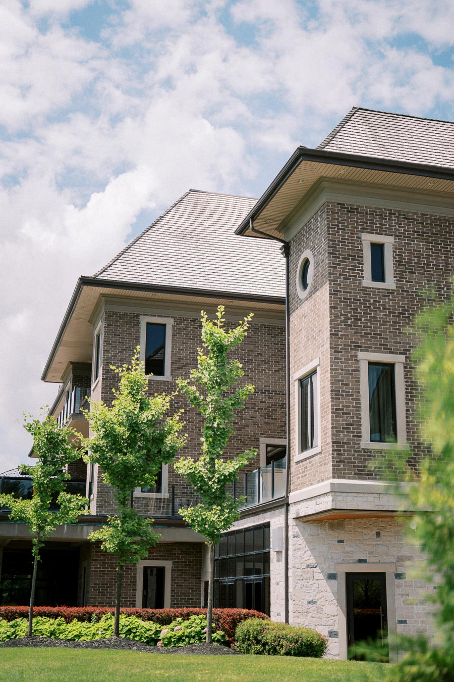 Modern brick building with large windows surrounded by lush green landscaping and clear blue sky.