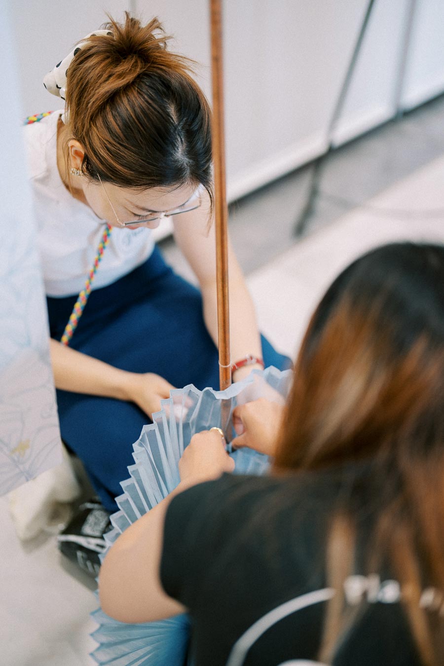 Two individuals engaging in a hands-on craft session involving intricate assembly of a blue pleated material, emphasizing teamwork and creativity, viewed from above.