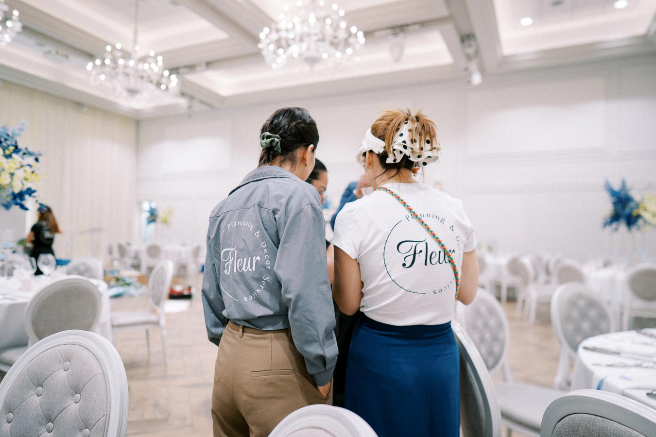 Two event planners from Fleur Planning & Decor Services in a beautifully decorated and elegant ballroom setting, preparing for an upcoming event.