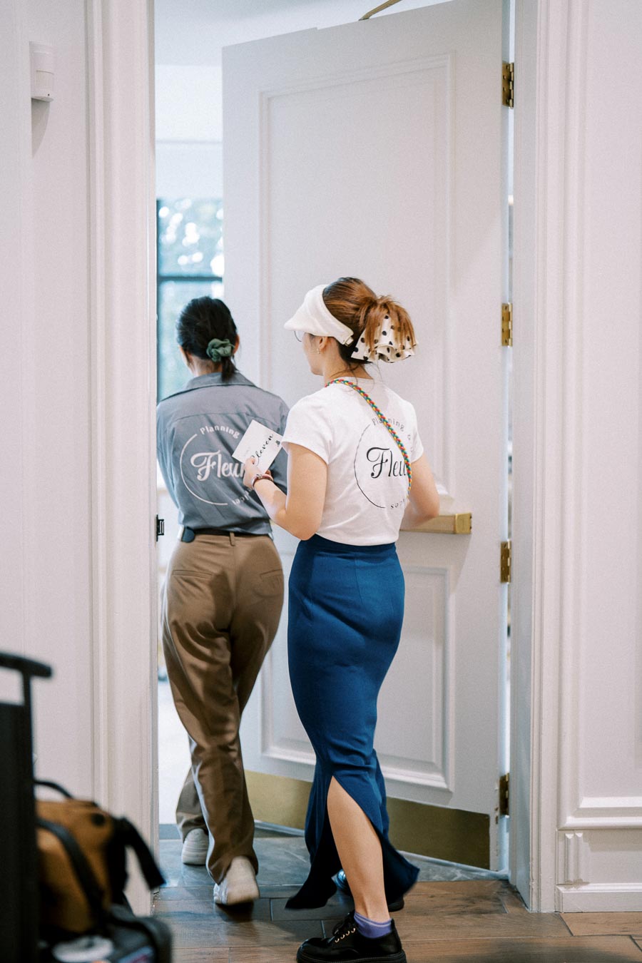 Two individuals in branded uniforms walking through a door, one holding a notebook, in a bright indoor setting.