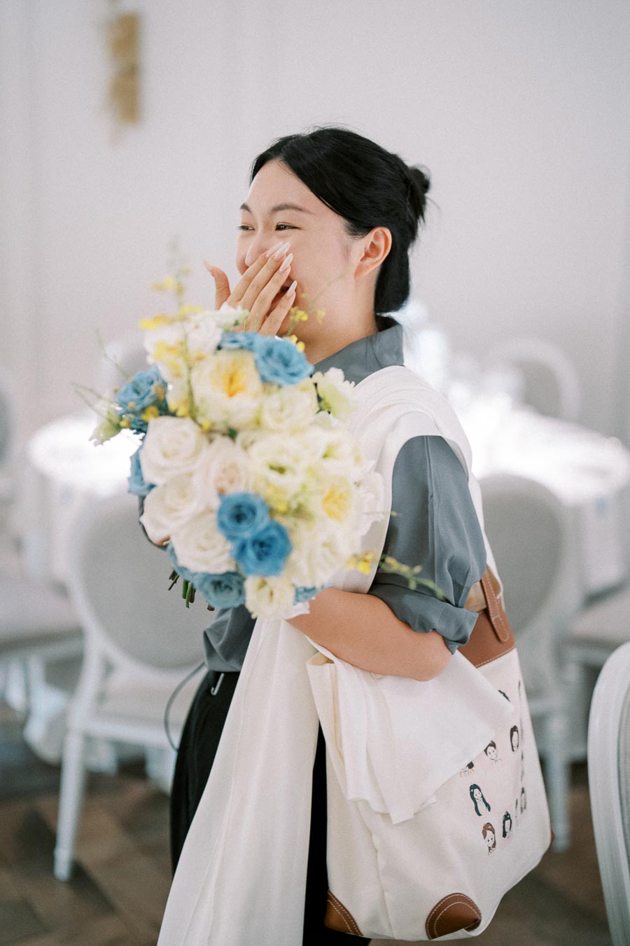 A woman smiling with joy holds a bouquet of blue and white flowers in a bright room.