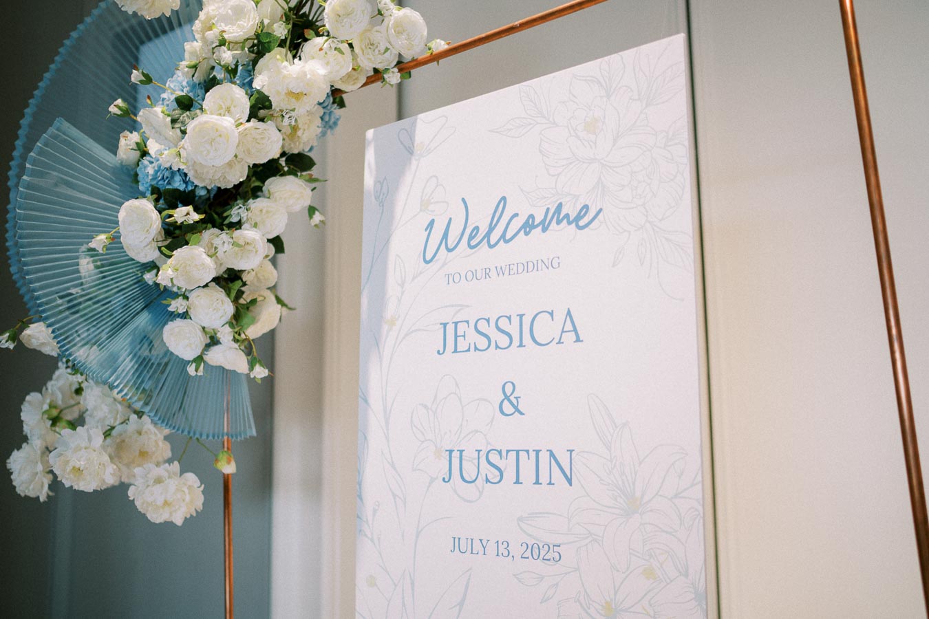 Wedding welcome sign with floral decorations, featuring white roses and blue accents, for Jessica and Justin's ceremony on July 13, 2025.