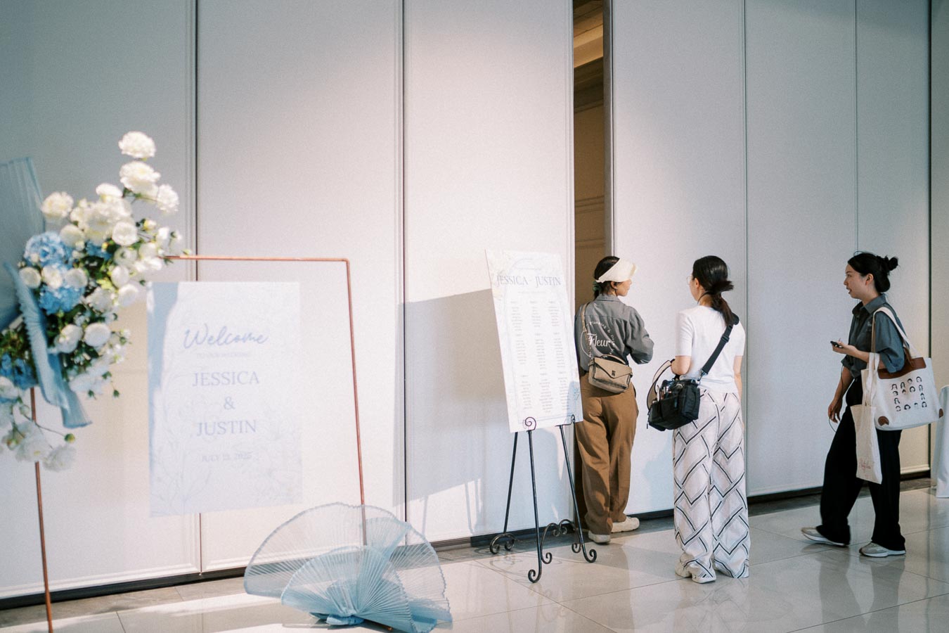 Three guests standing near a welcome sign adorned with flowers at Jessica and Justin's elegant wedding reception entrance.