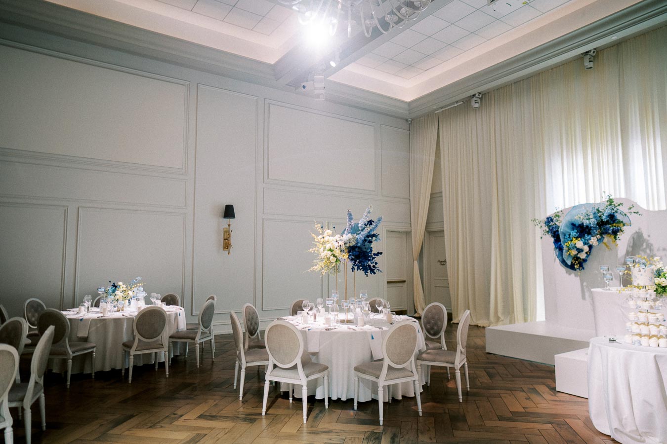 Elegant wedding reception venue with white table settings, floral centerpieces, and soft lighting.