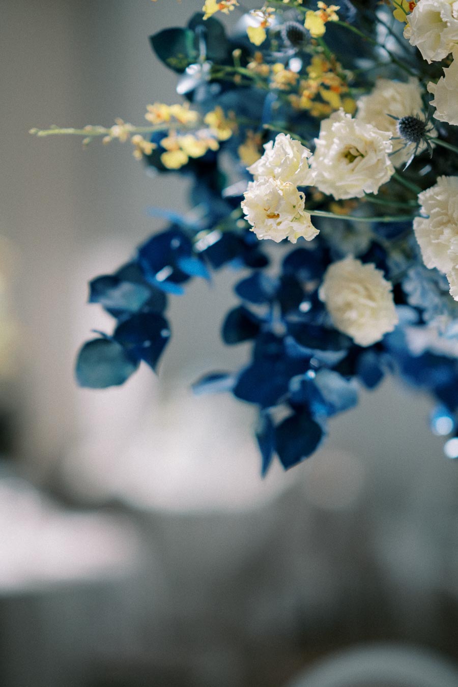 Elegant floral arrangement featuring white roses and blue leaves, accented with small yellow flowers, creating a delicate and sophisticated aesthetic.