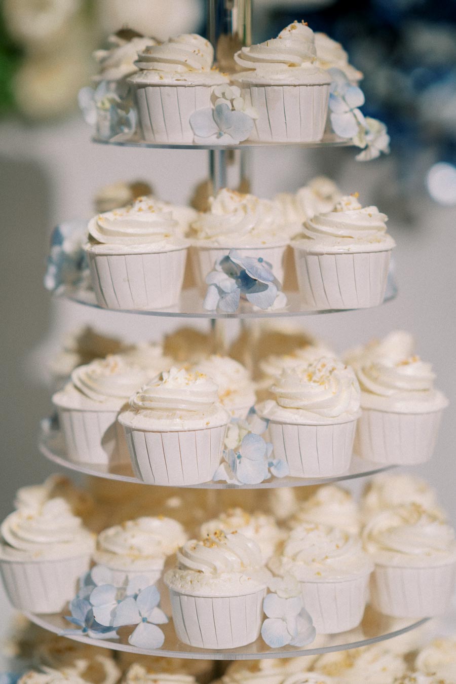 Tiered cupcake stand with elegant white-frosted cupcakes decorated with light blue flowers, perfect for weddings or special events.