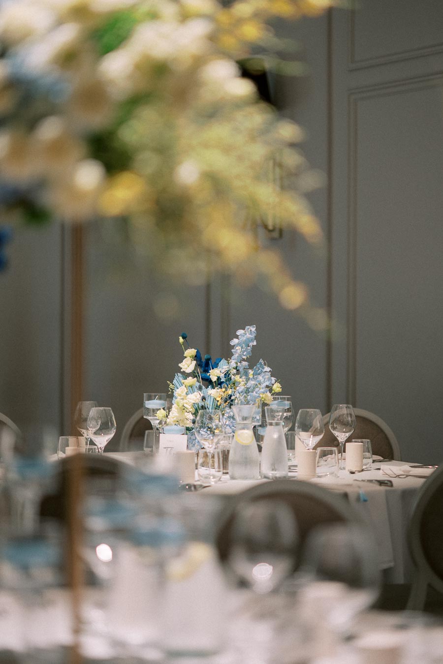 Elegant wedding reception table setting with a centerpiece of blue and white flowers, surrounded by glassware and candles, creating a romantic and sophisticated atmosphere.