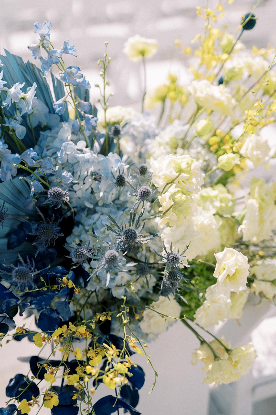 A beautiful floral arrangement featuring a mix of blue, white, and yellow blooms including hydrangeas, roses, and thistles, creating an elegant and vibrant display perfect for weddings or special events.