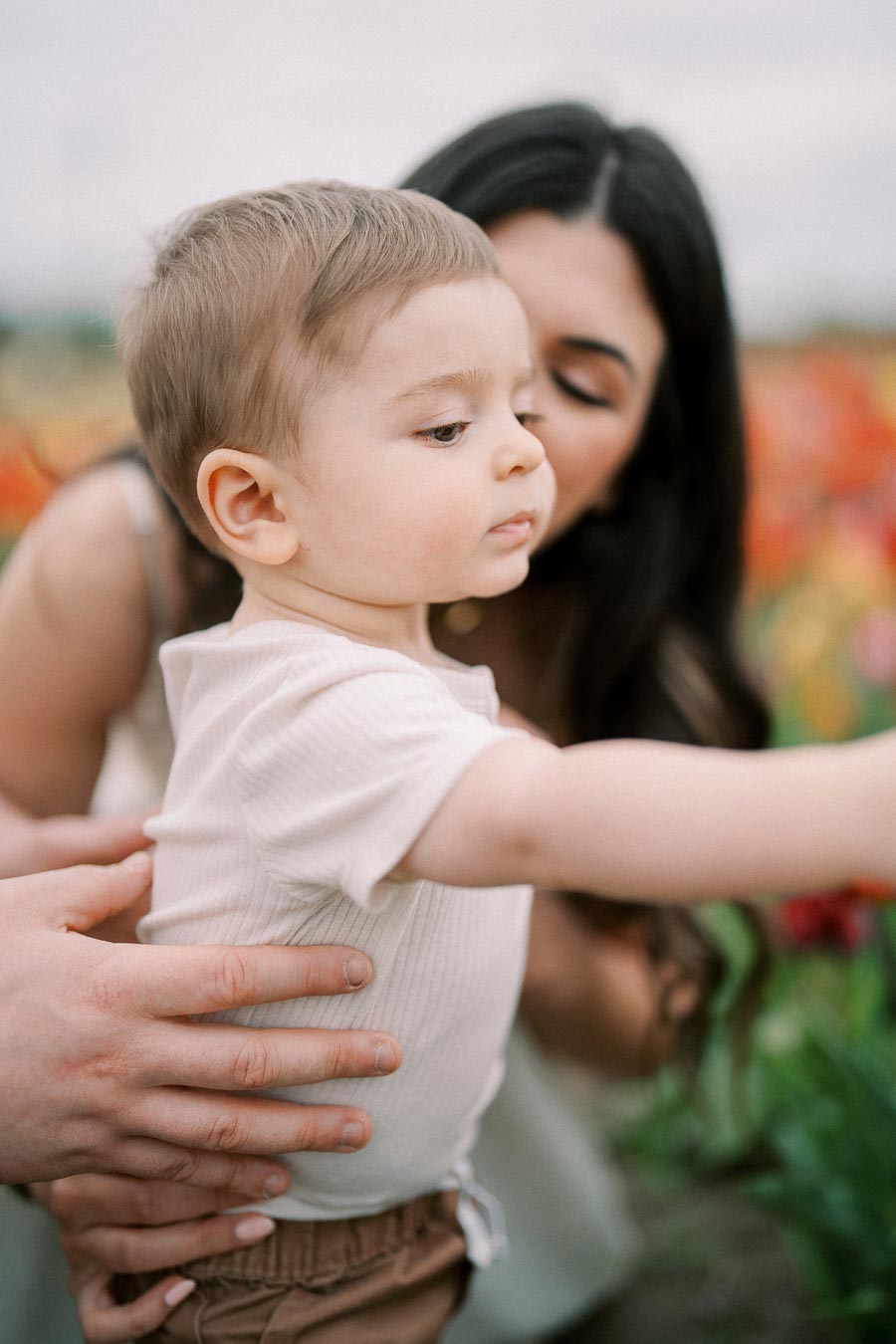 A woman gently holds a baby in a field of colorful flowers, capturing a tender moment.